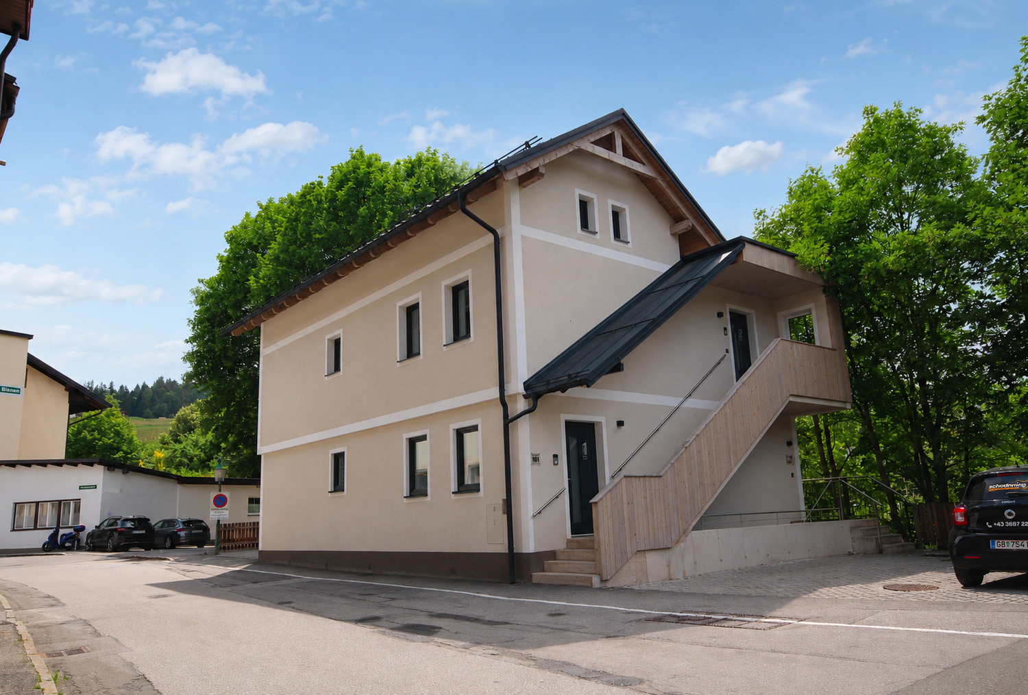 Two-story beige building with an outdoor wooden staircase beside trees