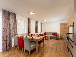 Open-plan dining area with red chairs and grey sofa.