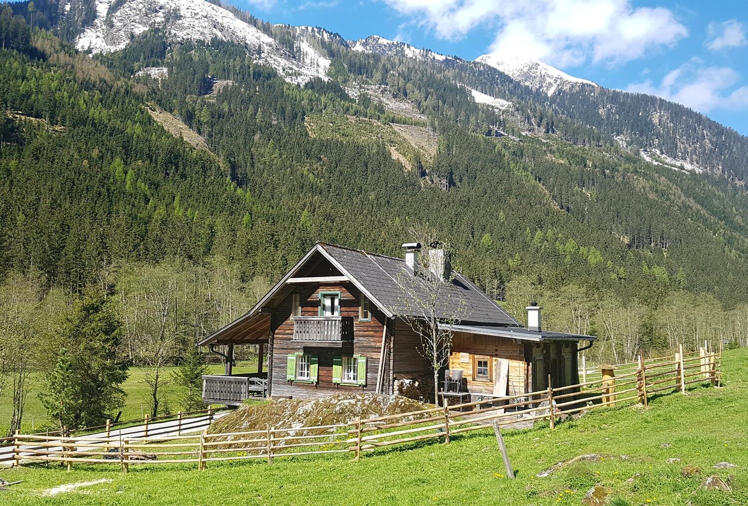 Holzhaus im Alpenstil auf grünem Weideland mit schneebedeckten Gipfeln