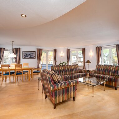 Spacious living and dining room with plaid sofas and wooden furniture