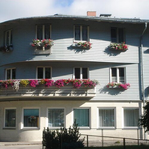 Weißes, gebogenes Wohnhaus mit Balkonen und Blumen