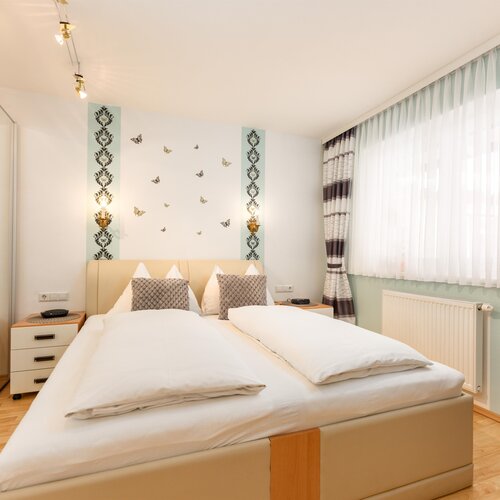 Hotelzimmer mit großem Bett, beigem Kopfteil, zwei Nachttischen