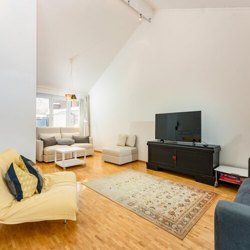 Helles Wohnzimmer mit gelbem Sessel, grauen Sofas und Fernseher