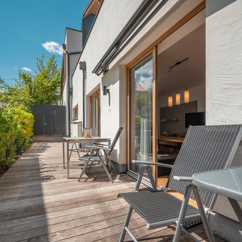 Outdoor wooden deck with seating beside a white building | © TIEBER