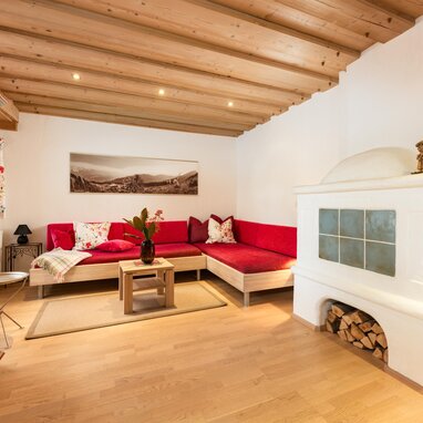 Gemütliches Wohnzimmer mit roten Sofas, Holzschrank und Kachelofen