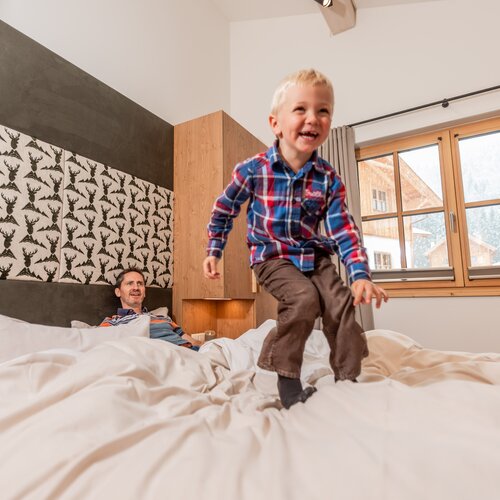 Kind springt auf dem Bett, während ein Mann zusieht | © C.Hoeflehner