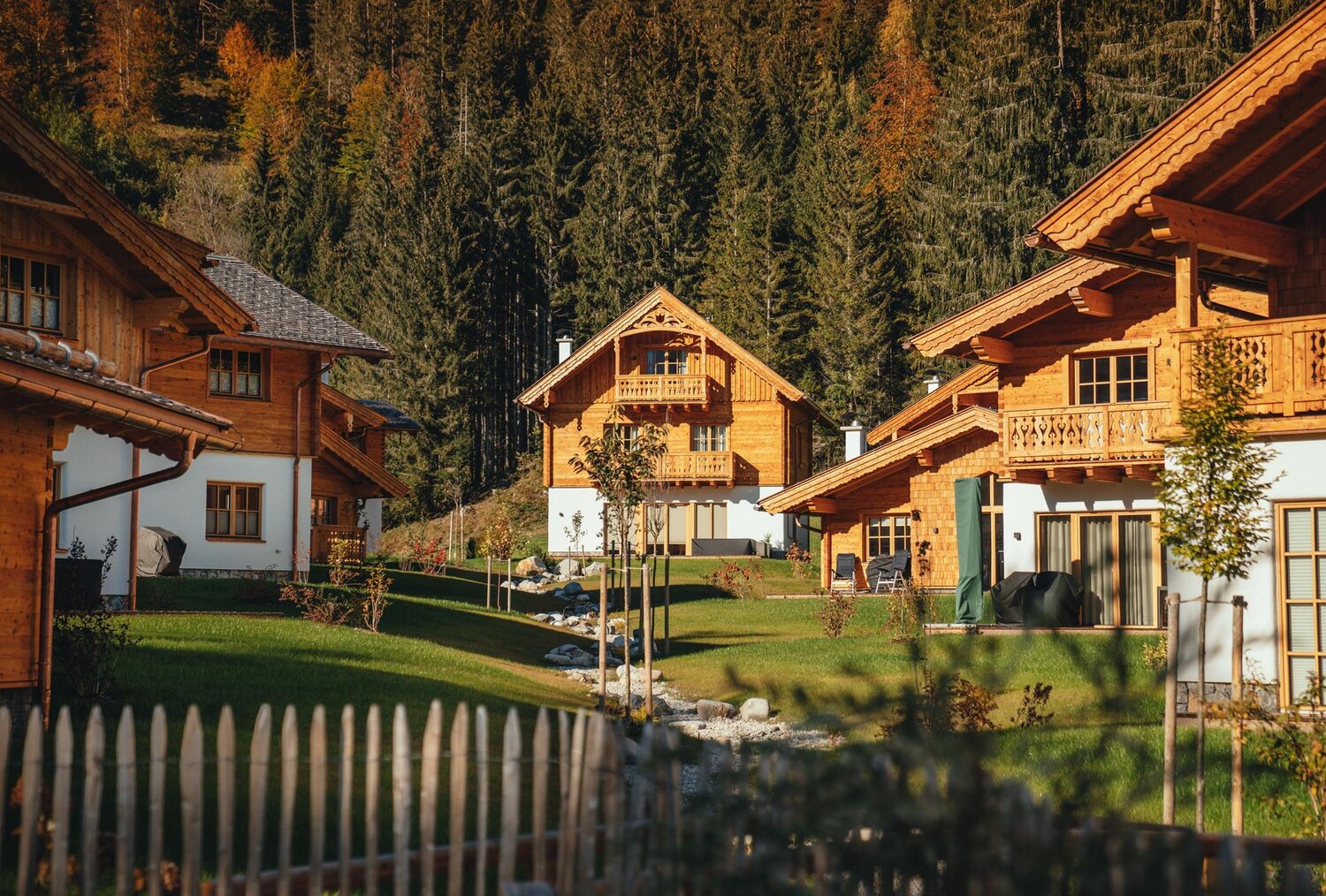 Row of wooden alpine chalets beside green lawn and trees