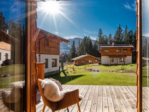 Blick vom Holzdeck auf ein sonniges alpines Dorf.