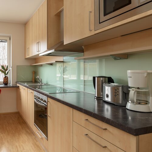 Modern kitchen with light wood cabinets, glass backsplash, and appliances