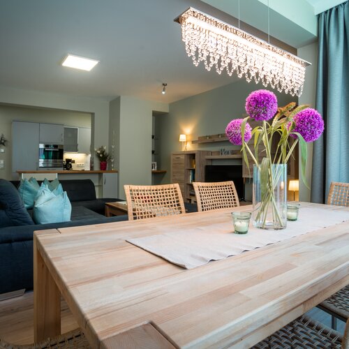 Open-plan dining area with wooden table, wicker chairs, and purple flowers | © Tieber Michael