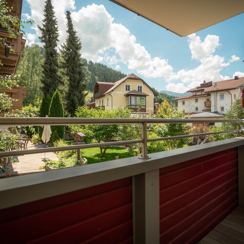 Balcony railing frames village houses, trees, and mountains. | © Tieber Michael