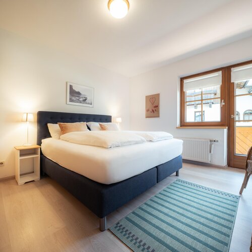 Helles Schlafzimmer mit Kingsize-Bett, blauem Kopfteil und Balkonfenstern | © TIEBER