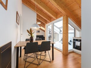 Bright dining area with wooden ceiling beams, large windows, and snow outside.