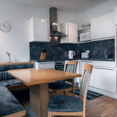 Moderne Küche mit weißen Schränken, dunkler Marmorrückwand und Esstisch