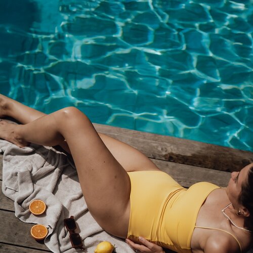 Person sonnt sich auf Holzdielen am Pool im gelben Badeanzug