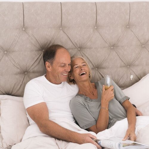 Lachendes älteres Paar im Bett, liest gemeinsam eine Zeitschrift