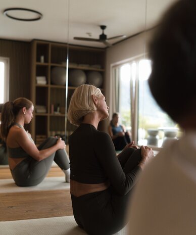 Woman in black athletic wear sits in yoga pose in mirrored studio