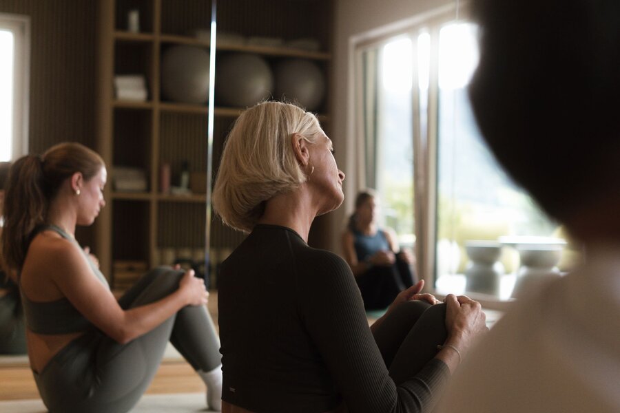 Woman in black athletic wear sits in yoga pose in mirrored studio