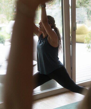 Frau macht High-Lunge-Yoga-Position drinnen vor Glasfront