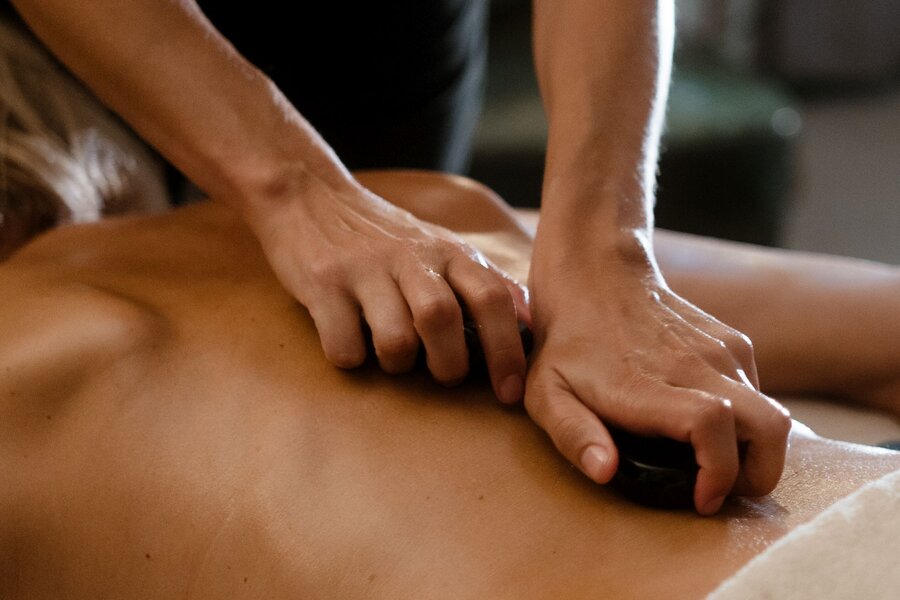 Massagetherapeut führt Hot-Stone-Massage am Rücken durch