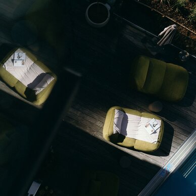Three olive-green lounge chairs on a wooden deck by a pool