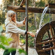 Mädchen berührt hölzernes Wasserrad im Wald