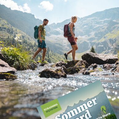 Zwei Wanderer überqueren einen felsigen Bach im Alpen Tal; Sommer card.